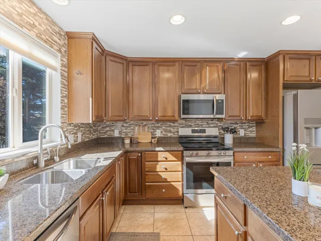 Kitchen with wood-finish cabinetry, stainless steel appliances, granite countertops, and a tile backsplash