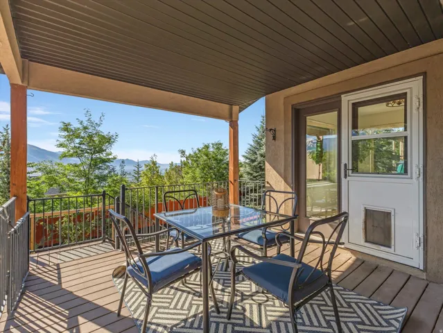Covered outdoor deck with wood-finish flooring, black metal railings, and a sliding glass door