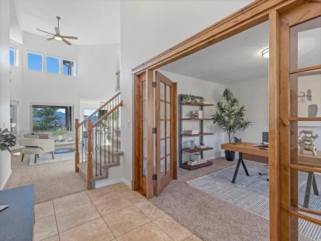 Two-story entry with a ceiling fan, a staircase featuring wood newel posts and wrought iron balusters, and a separate room with wood-frame French doors