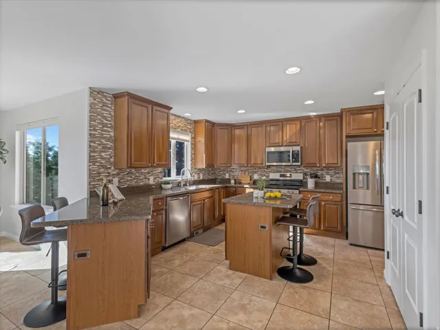 Kitchen featuring wood cabinetry, stainless steel appliances, tile flooring, and stone countertops with a mosaic tile backsplash