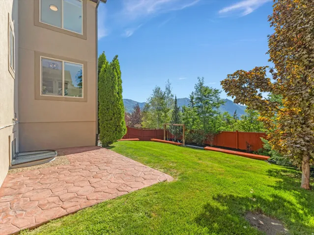 Expansive lawn area with a stamped concrete patio, a wood fence, and mature trees