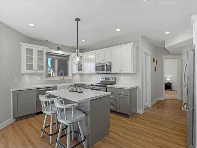 Kitchen featuring an island with stone countertop, wood-finish flooring, two-tone cabinetry, and recessed lighting