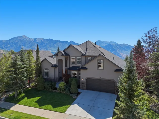 Stucco exterior with stone accents, mature landscaping, concrete driveway, and a two-car garage