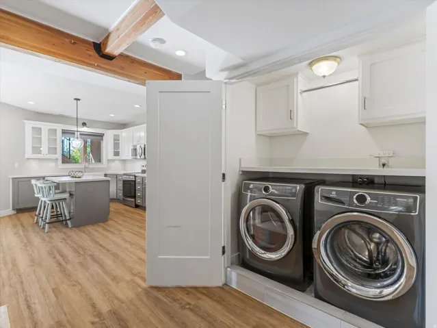 Convenient laundry area with built-in cabinetry and counter space, complemented by wood-finish flooring extending into the kitchen with a central island and white upper cabinetry