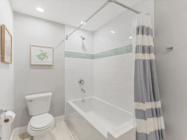 Recessed lighting, white subway tile surround, integrated bathtub, and a modern toilet