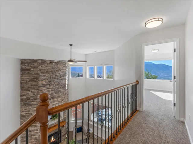 Stoned-faced fireplace with wood mantel, three upper windows, and a ceiling fan