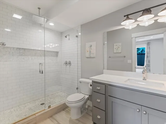 Glass-enclosed shower with white subway tile, mosaic shower floor, and ceiling-mounted rain shower head