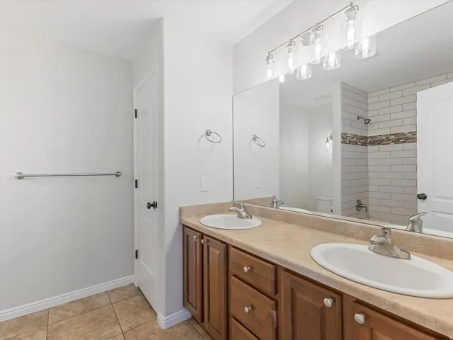 Dual vanity with wood-finish cabinetry and integrated sinks, brushed nickel fixtures, and a large mirror