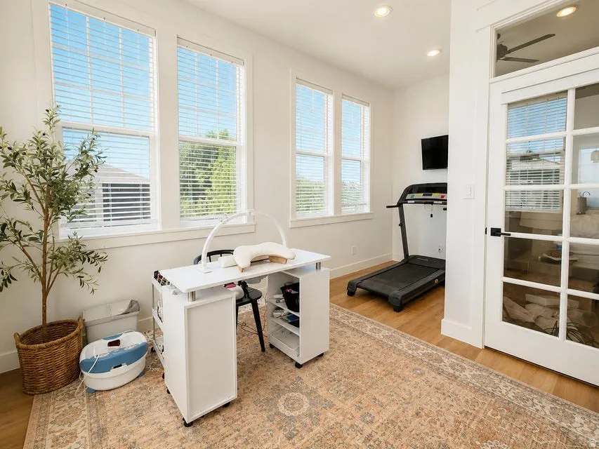 Multiple large windows, wood-finish flooring, recessed ceiling lighting, and a white interior door with glass panels