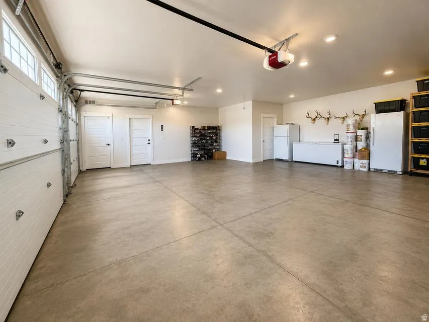 Spacious garage featuring a concrete floor, two white garage doors with upper window panels, and recessed ceiling lighting