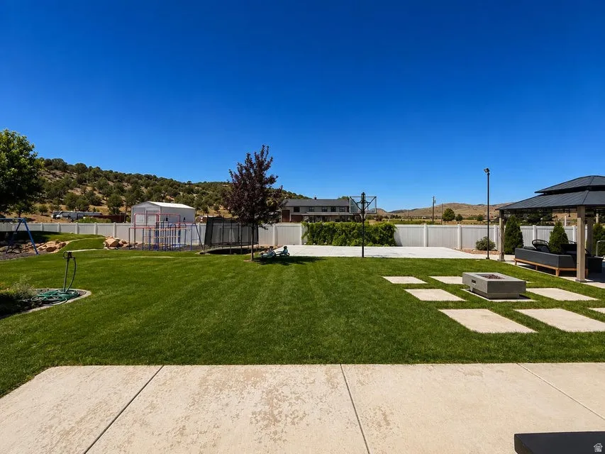 Expansive backyard featuring a lush lawn, concrete patio, stepping stones, a built-in fire pit, and a covered gazebo