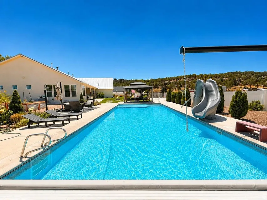 Expansive outdoor pool with integrated slide, rope swing, and surrounding hardscaping