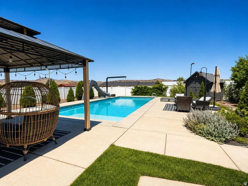 Outdoor swimming pool with integrated slide, concrete patio, a covered pergola, and a detached shed