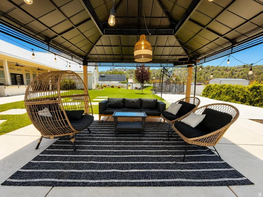 Outdoor patio featuring a black metal gazebo with integrated lighting, concrete paver flooring, and a large manicured lawn
