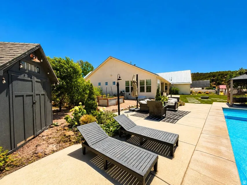 Concrete patio with an integrated swimming pool, a standalone storage shed, raised garden beds, and a manicured lawn
