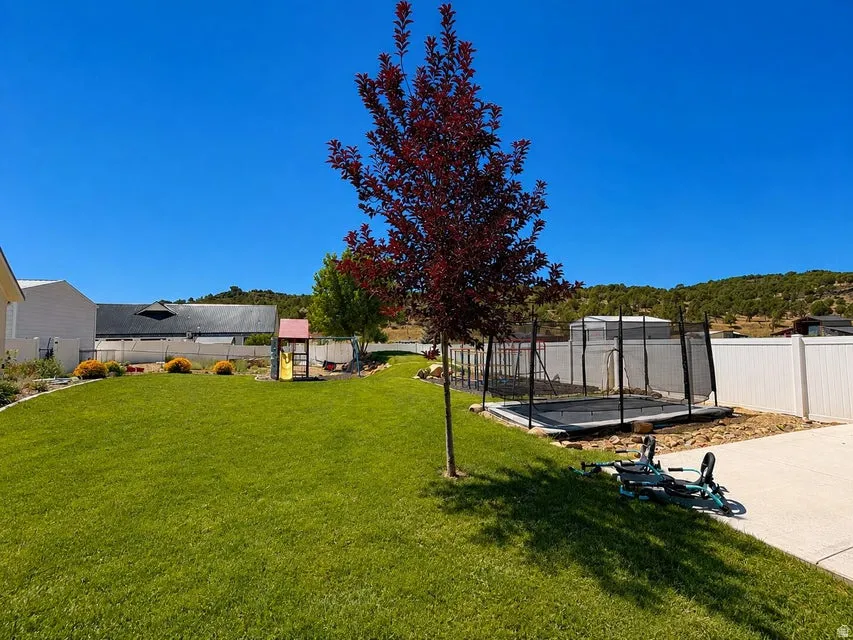 Expansive grassy backyard featuring a built-in trampoline, a paved patio, and a white privacy fence