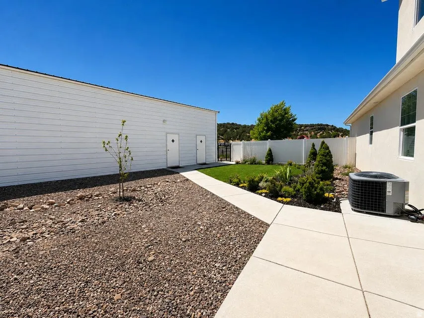 Concrete pathways, gravel landscaping, manicured lawn, white privacy fence, and mature shrubs