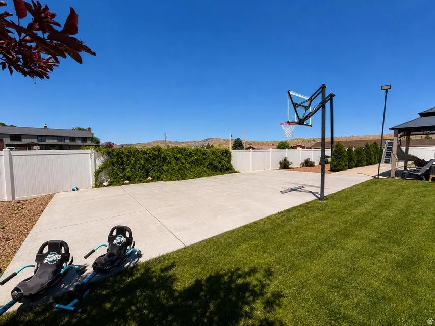 Expansive backyard featuring a large concrete pad, basketball hoop, and a covered gazebo