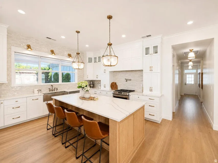 Kitchen featuring a large island with a quartz countertop, wood-finish flooring, white cabinetry, a tile backsplash, and a stainless steel farmhouse sink