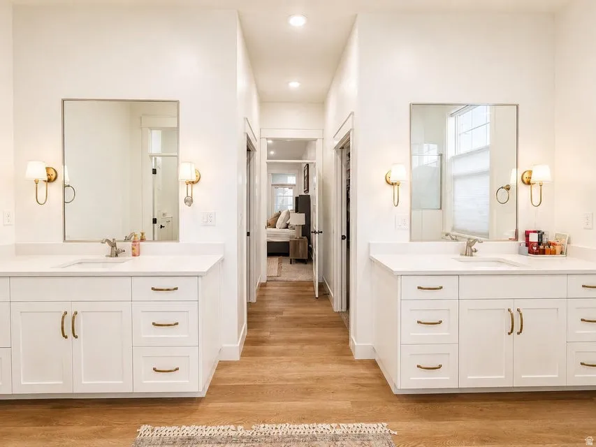 Dual vanities with white cabinetry, gold-finish hardware, and wall sconces