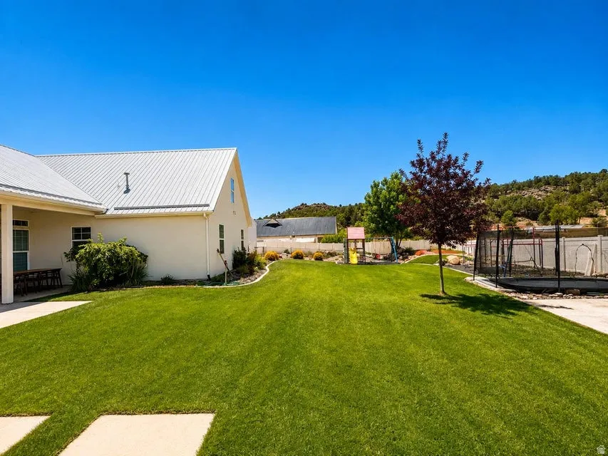 Expansive green lawn, stucco exterior, metal roof, mature trees, and a concrete patio