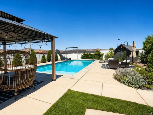 Outdoor swimming pool with integrated slide, concrete patio, a covered pergola, and a detached shed