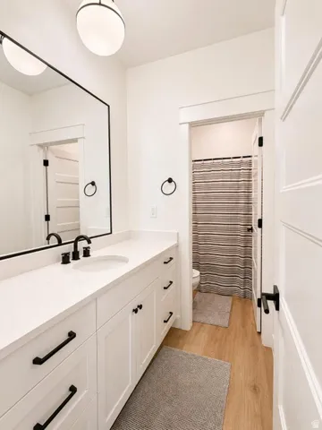 Elongated single vanity with a white countertop and white cabinetry, integrated sink, matte black faucet, and wood-finish flooring