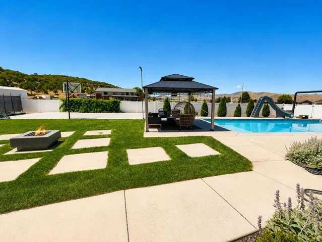 Expansive outdoor space featuring a swimming pool, concrete patio, built-in fire pit, and a gazebo