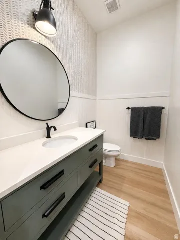 Vanity with a basin sink and matte black faucet, wall-mounted mirror, accent wallpaper, and wood-finish flooring