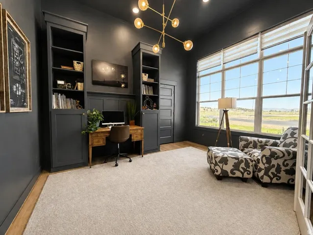 Built-in shelving with lower cabinetry, decorative wall paneling, large multi-pane windows, wood-finish flooring, and a modern chandelier