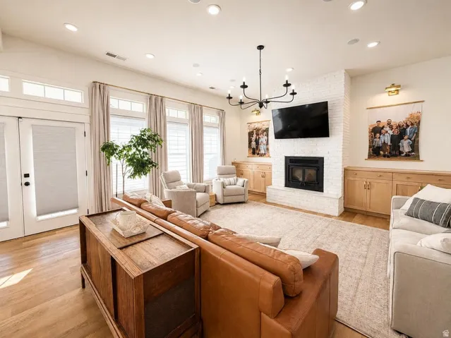 Spacious living area featuring wood-finish flooring, a white brick fireplace, built-in cabinetry, recessed lighting, and a contemporary chandelier