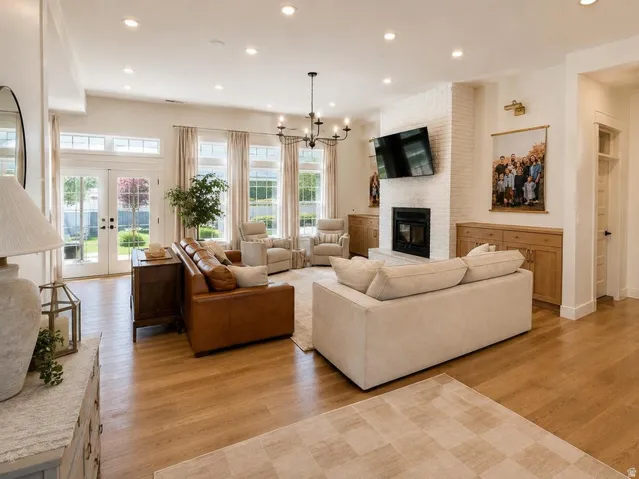 Recessed lighting, wood-finish flooring, white brick fireplace, built-in wooden cabinetry, and double French doors to the exterior