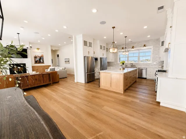 Open-concept living area with wood-finish flooring, a white brick fireplace, and recessed lighting