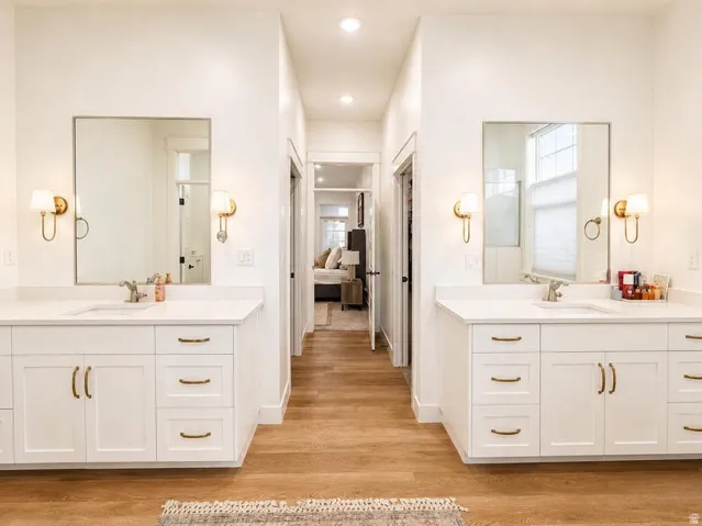 Dual vanities with white cabinetry, gold-finish hardware, and wall sconces