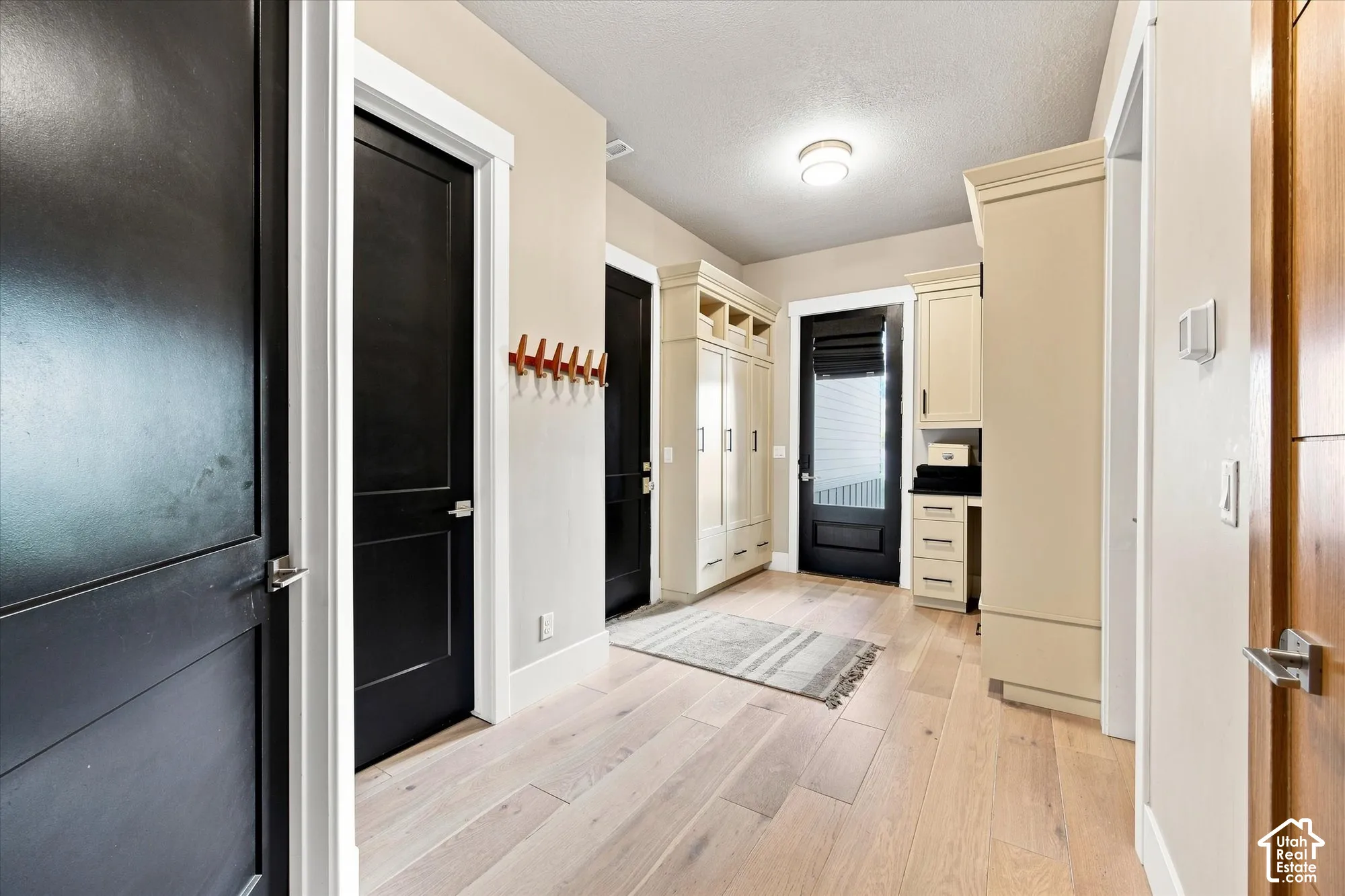 Garage Entry. Light wood-finish flooring, built-in cabinetry with open shelving, and dark panel doors with contemporary hardware
