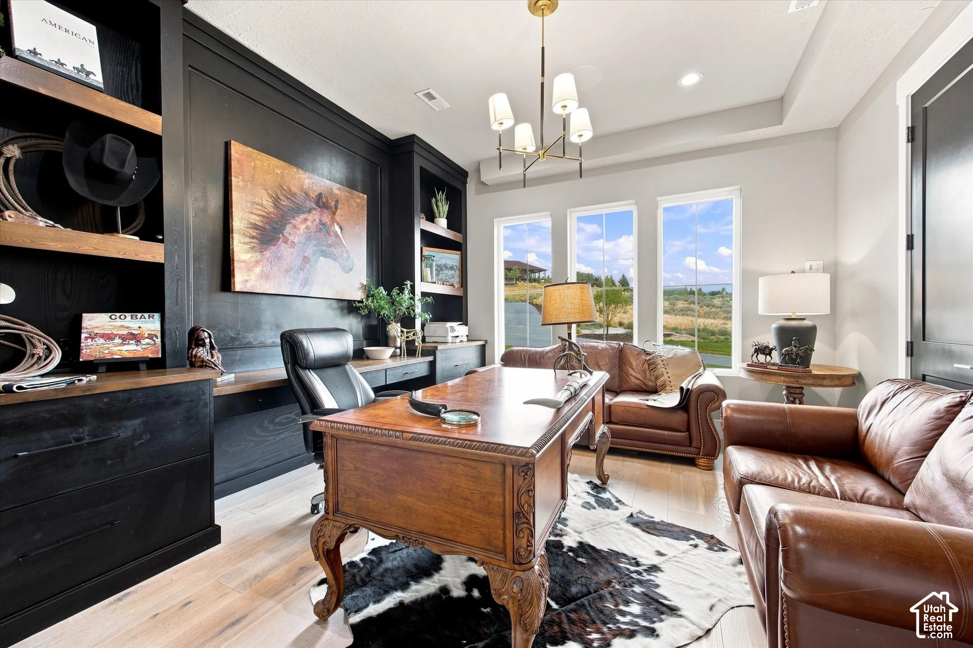 Custom built-in shelving, light wood-finish flooring, three large windows, a tray ceiling, and a contemporary chandelier