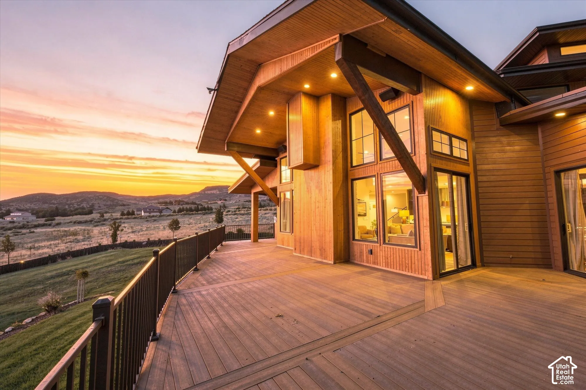 Expansive composite deck with dark metal railing, featuring a wood-clad exterior, multiple large windows, and sliding glass doors