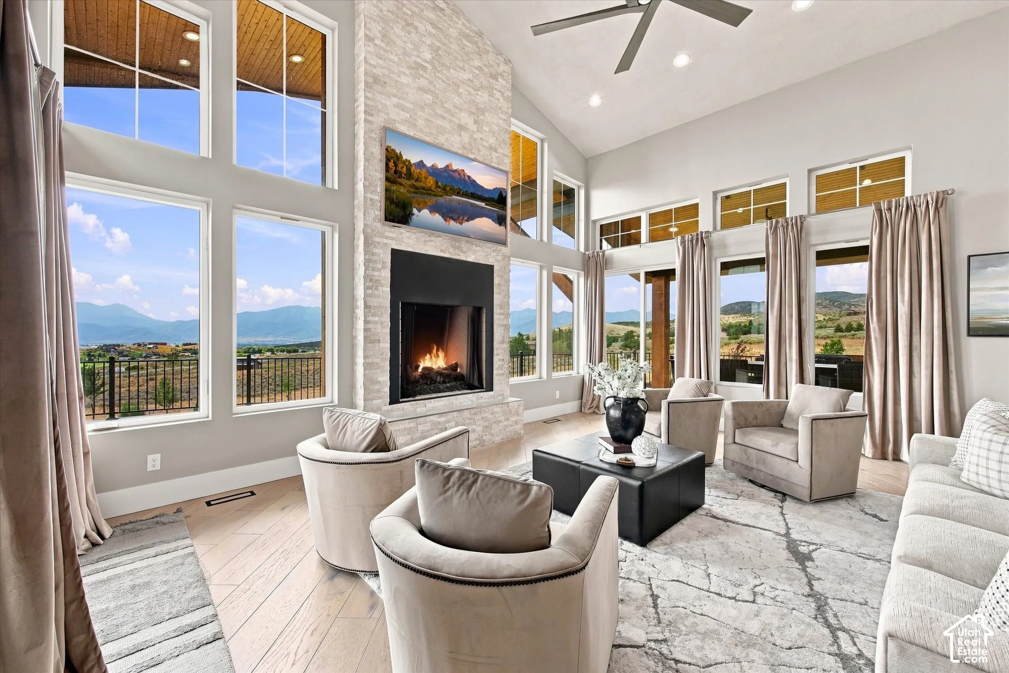 Vaulted ceiling with recessed lighting, floor-to-ceiling windows, stone-clad fireplace with a black surround, wood-finish flooring, and a ceiling fan