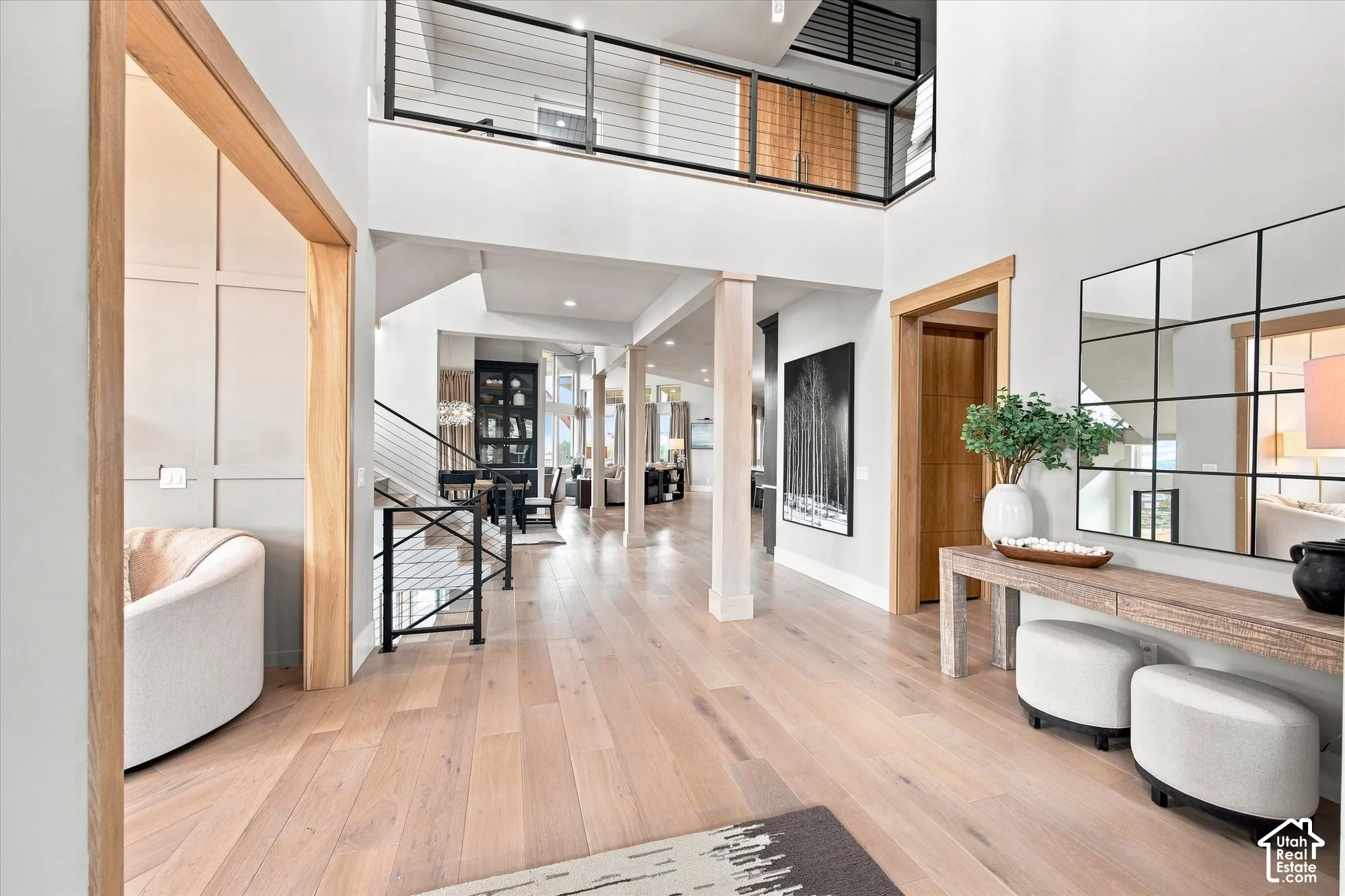 Grand entryway featuring light wood-finish flooring, a double-height ceiling, and a prominent open staircase with black metal railings