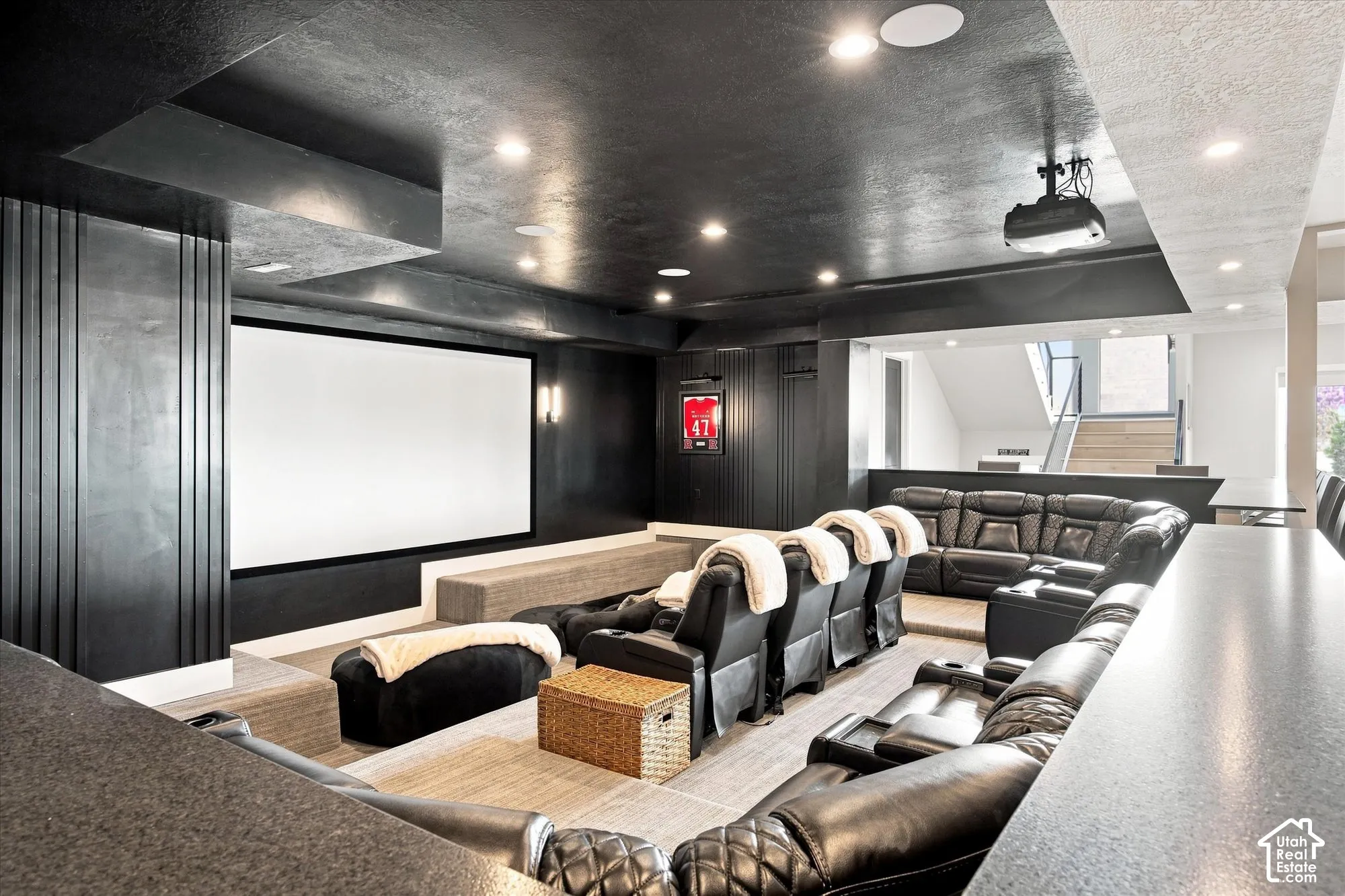 Integrated projector and screen, tiered seating, built-in counter, recessed lighting, and a partial staircase