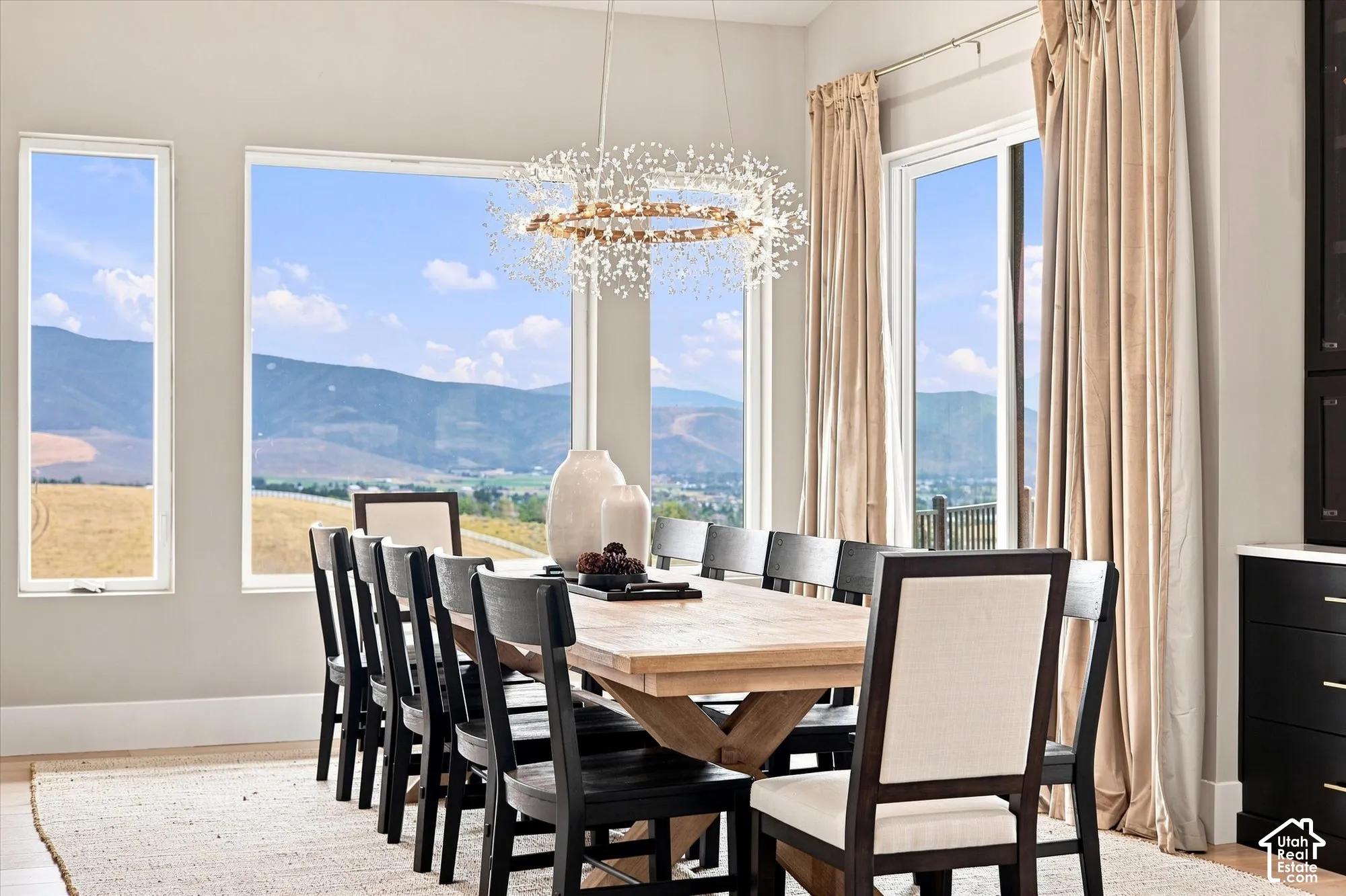 Expansive window wall with mountain scenery, modern chandelier, light wood-finish flooring, and built-in cabinetry with stone countertop