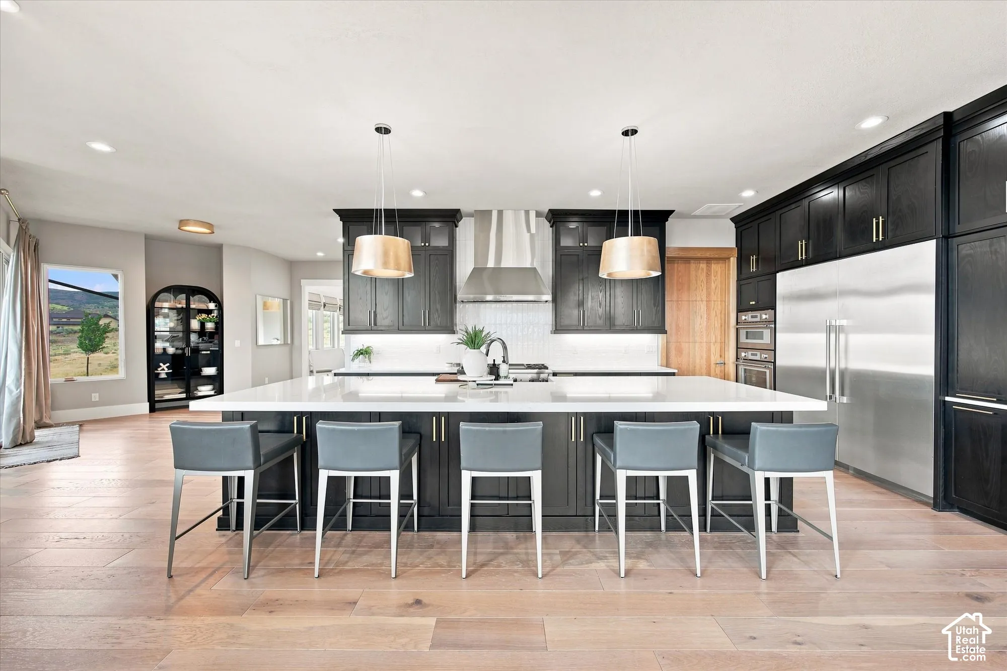 Expansive kitchen island with seating, dark wood cabinetry, stainless steel appliances, light wood-finish flooring, and pendant lighting