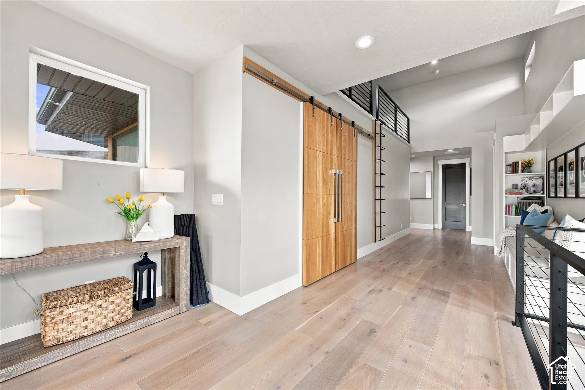 Wood-finish flooring throughout, barn door with a horizontal panel design, open shelving, built-in window seating, and a loft with black metal railing