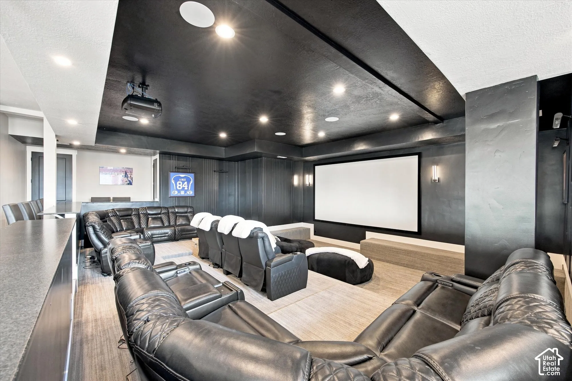 Home Theater featuring a projection screen, tiered seating with leather recliners, wood-finish flooring, recessed lighting throughout, and a black coffered ceiling with integrated acoustic treatment