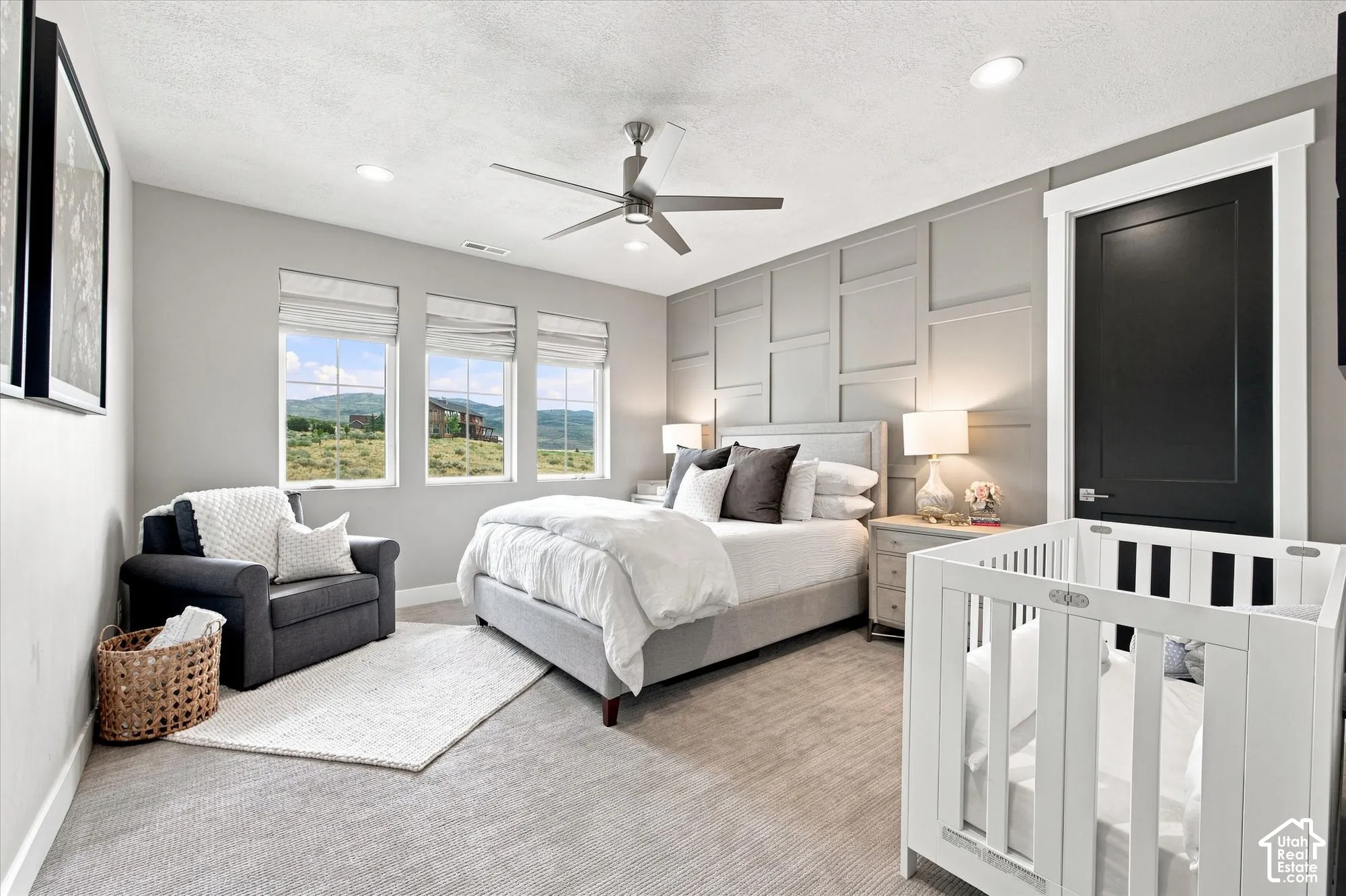 Accent wall with decorative paneling, recessed lighting, ceiling fan with light fixture, three windows with roman shades, and a dark panel door with white trim