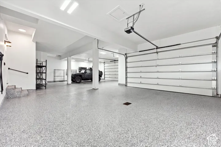 Spacious 4 bay garage featuring a durable epoxy floor, multiple overhead doors, recessed lighting, and structural support beams