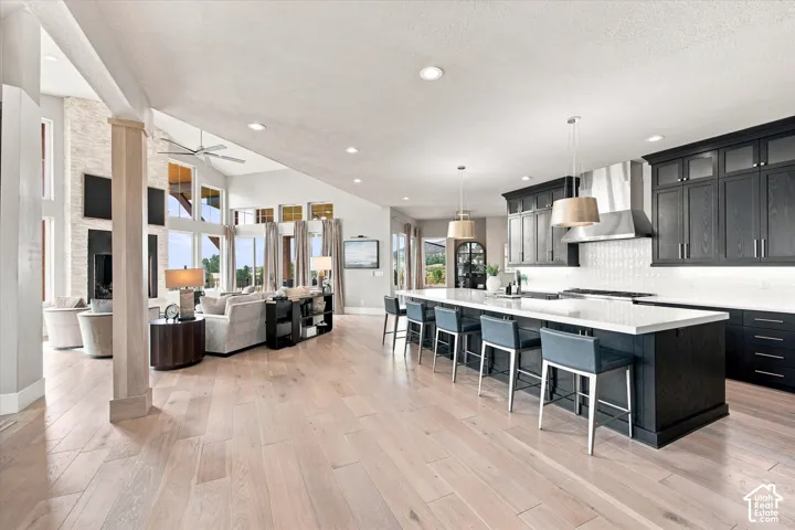 Open-concept living space with light wood-finish flooring, a kitchen island with seating, dark-toned cabinetry, and a living area with a vaulted ceiling