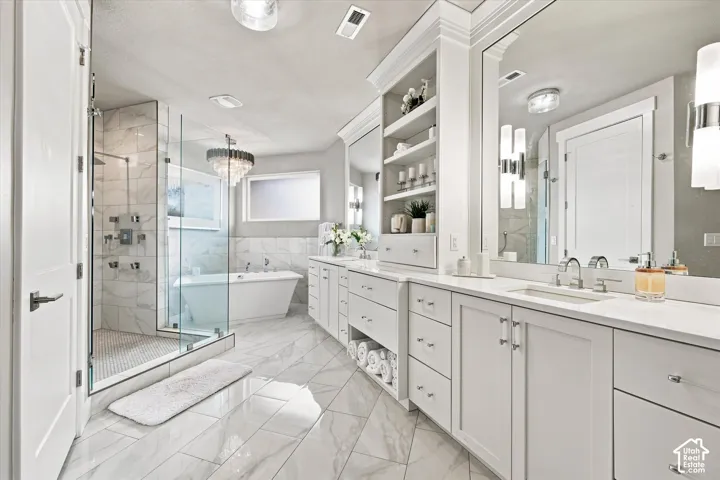 Primary En-suite bathroom featuring a frameless glass shower enclosure, freestanding soaking tub, dual vanity with white cabinetry, and large format marble-look tile flooring