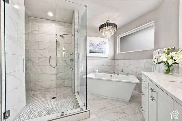 Primary En-suite bathroom featuring a freestanding tub, glass-enclosed shower with multiple showerheads, marble-patterned tile, and a vanity with an integrated sink
