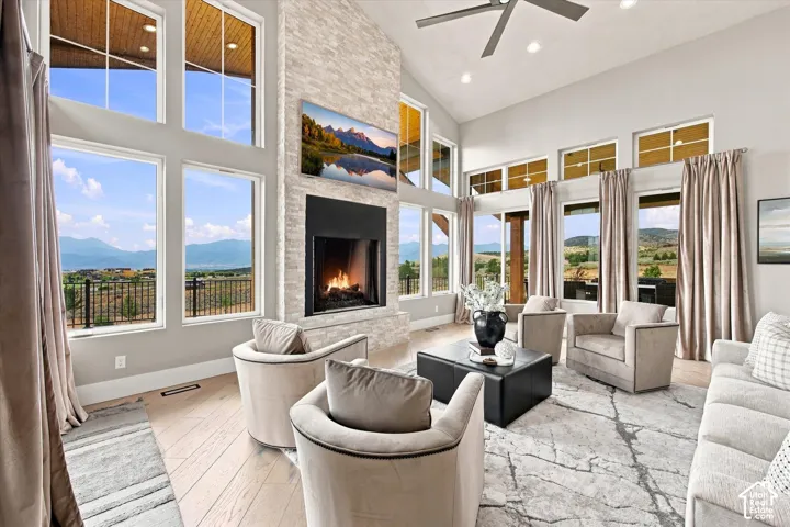 Vaulted ceiling with recessed lighting, floor-to-ceiling windows, stone-clad fireplace with a black surround, wood-finish flooring, and a ceiling fan